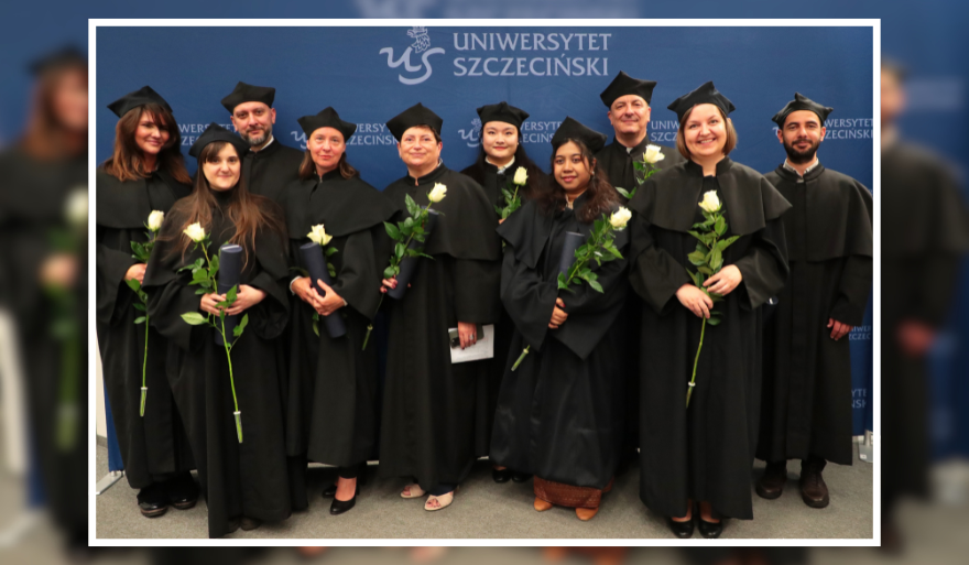 A group of ten people in black academic gowns and mortarboards stands in front of a backdrop with the logo and inscription “University of Szczecin”. Each person is holding a white rose, and some are also holding rolled documents.